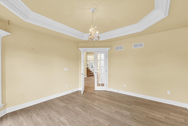 empty room with a tray ceiling, wood-type flooring, crown molding, and a notable chandelier