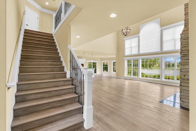 stairway featuring a high ceiling, wood-type flooring, a chandelier, and ornamental molding