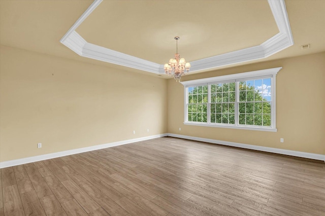 empty room featuring crown molding, a chandelier, a raised ceiling, and baseboards