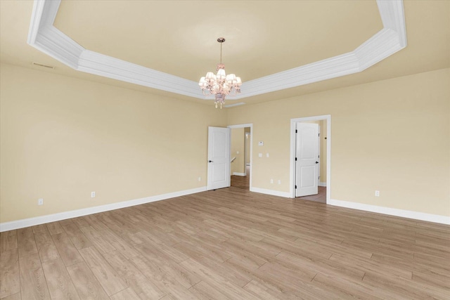 spare room featuring an inviting chandelier, light wood finished floors, a raised ceiling, and ornamental molding