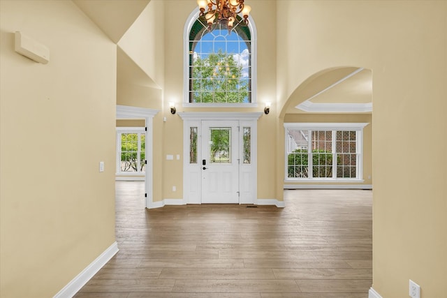 foyer entrance featuring crown molding, hardwood / wood-style flooring, an inviting chandelier, and a high ceiling