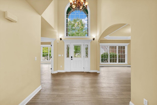 foyer entrance featuring arched walkways, an inviting chandelier, wood-type flooring, baseboards, and a high ceiling