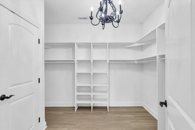 spacious closet featuring wood finished floors, visible vents, and a notable chandelier