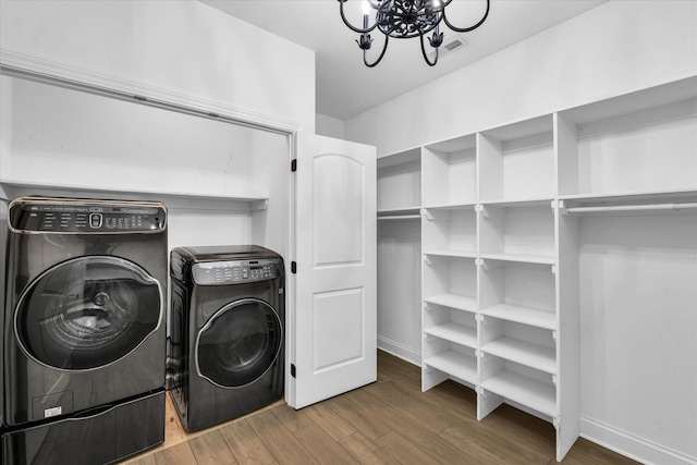 washroom with an inviting chandelier, washer and clothes dryer, and light hardwood / wood-style flooring