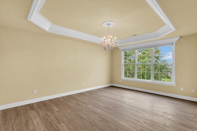 empty room with wood finished floors, an inviting chandelier, ornamental molding, baseboards, and a raised ceiling