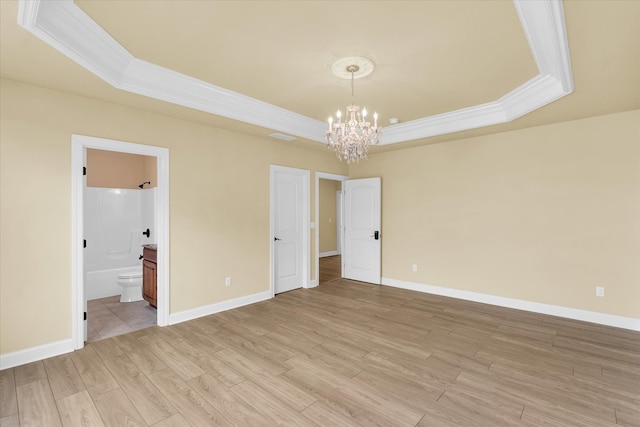 unfurnished bedroom featuring a raised ceiling, light hardwood / wood-style floors, ornamental molding, and ensuite bath