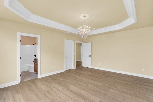 unfurnished room featuring a chandelier, ornamental molding, light wood finished floors, and a tray ceiling