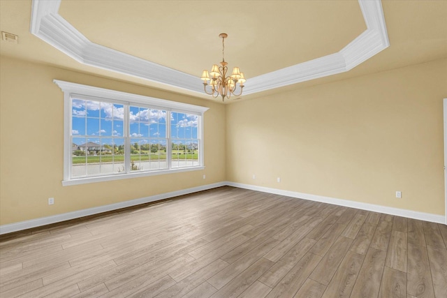 spare room featuring a notable chandelier, a tray ceiling, baseboards, ornamental molding, and wood finished floors