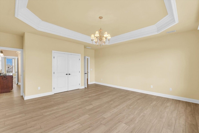 empty room with ornamental molding, a notable chandelier, a raised ceiling, and light wood-type flooring