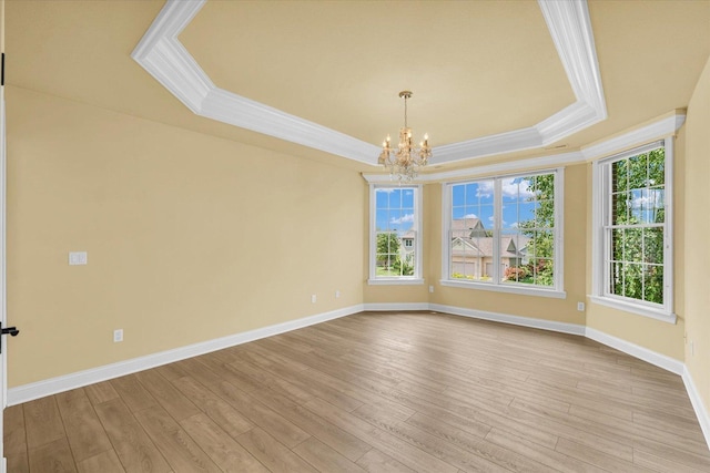 spare room featuring light wood-style flooring, ornamental molding, baseboards, a raised ceiling, and a notable chandelier