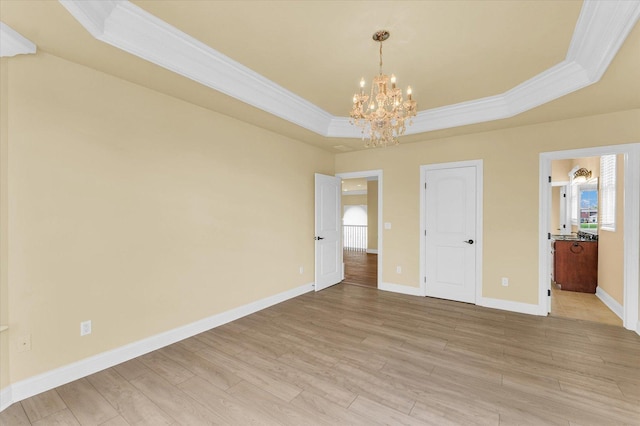 interior space with light wood finished floors, a chandelier, a raised ceiling, baseboards, and ornamental molding