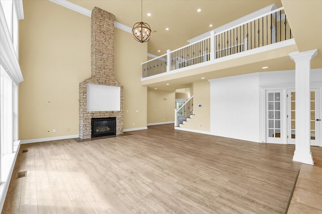 unfurnished living room with a fireplace, an inviting chandelier, crown molding, light hardwood / wood-style flooring, and a high ceiling