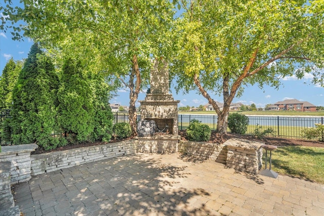 view of patio with an outdoor stone fireplace, a water view, and a fenced backyard