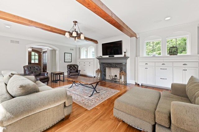 living room featuring a fireplace, beamed ceiling, crown molding, light hardwood / wood-style flooring, and an inviting chandelier