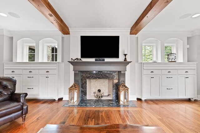 living room featuring crown molding, a premium fireplace, beamed ceiling, and light hardwood / wood-style floors