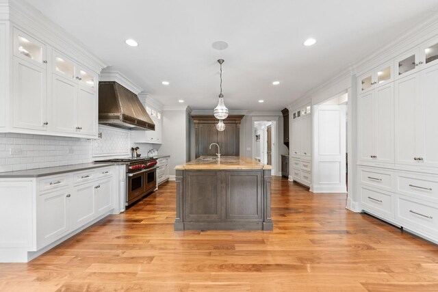 kitchen featuring light wood-type flooring, sink, wall chimney range hood, range with two ovens, and pendant lighting