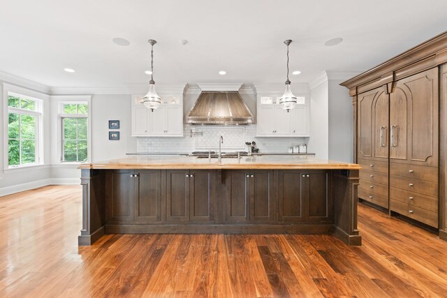 kitchen featuring white cabinets, custom exhaust hood, dark hardwood / wood-style flooring, a center island with sink, and butcher block counters