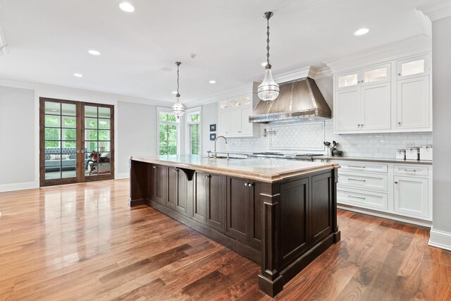 kitchen featuring pendant lighting, custom range hood, wood-type flooring, and a kitchen island with sink