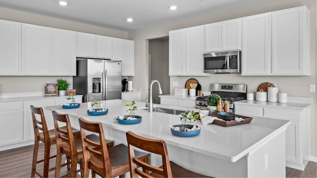 kitchen with a kitchen breakfast bar, sink, appliances with stainless steel finishes, hardwood / wood-style flooring, and a center island with sink