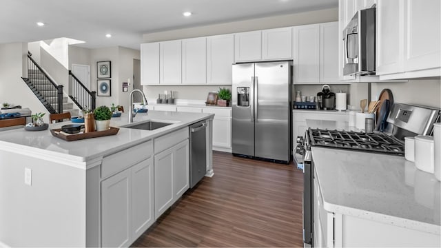 kitchen with appliances with stainless steel finishes, white cabinetry, sink, dark hardwood / wood-style floors, and a kitchen island with sink