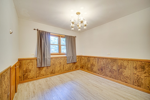 empty room with wood walls, hardwood / wood-style flooring, and an inviting chandelier