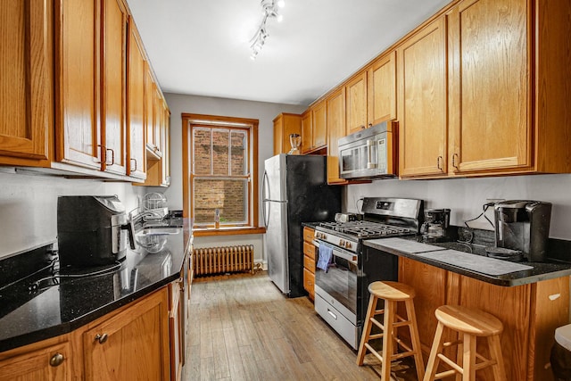 kitchen with radiator, stainless steel appliances, light wood-style floors, a kitchen breakfast bar, and brown cabinets