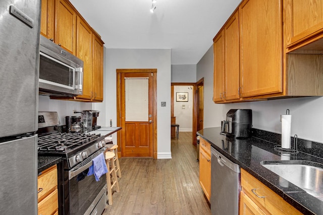 kitchen featuring dark stone countertops, appliances with stainless steel finishes, brown cabinetry, and light wood finished floors