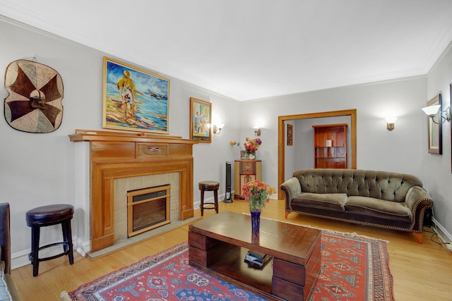 living room with a tile fireplace, baseboards, crown molding, and light wood-style floors