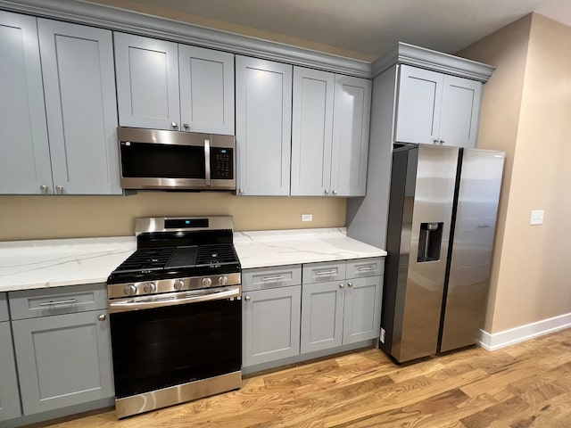 kitchen with gray cabinetry, light stone countertops, stainless steel appliances, and light hardwood / wood-style floors