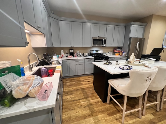 kitchen with gray cabinetry, light hardwood / wood-style flooring, a breakfast bar, stainless steel appliances, and sink