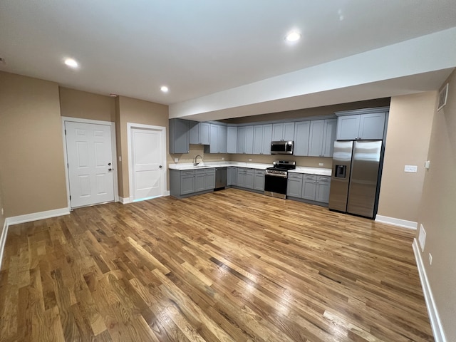 kitchen with gray cabinetry, stainless steel appliances, sink, and wood-type flooring