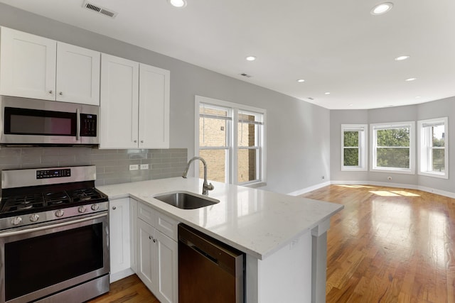 kitchen with kitchen peninsula, sink, light hardwood / wood-style flooring, appliances with stainless steel finishes, and white cabinetry