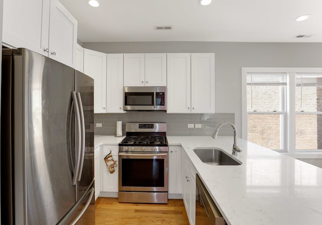 kitchen with white cabinets, sink, light hardwood / wood-style flooring, appliances with stainless steel finishes, and light stone counters