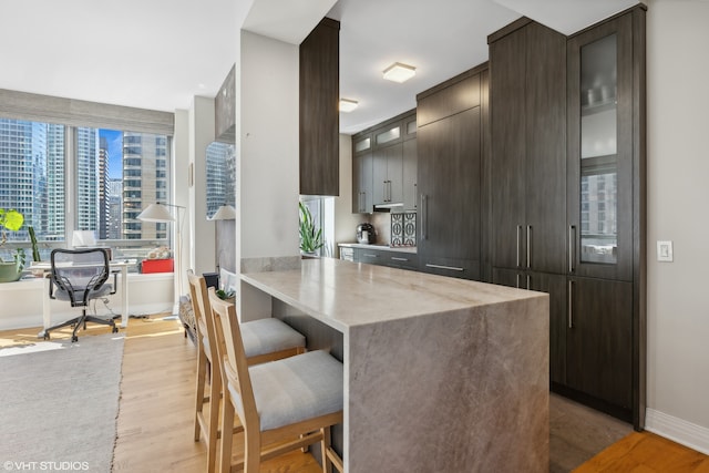 kitchen featuring a kitchen breakfast bar, light stone countertops, light hardwood / wood-style flooring, kitchen peninsula, and dark brown cabinetry