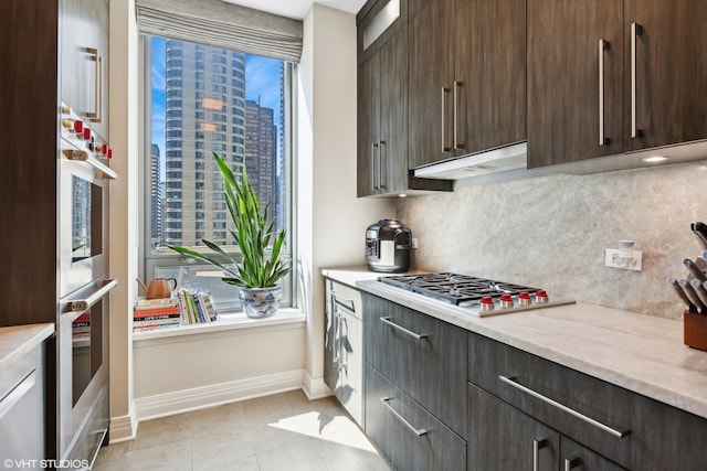 kitchen with light tile patterned floors, backsplash, stainless steel gas cooktop, and dark brown cabinetry