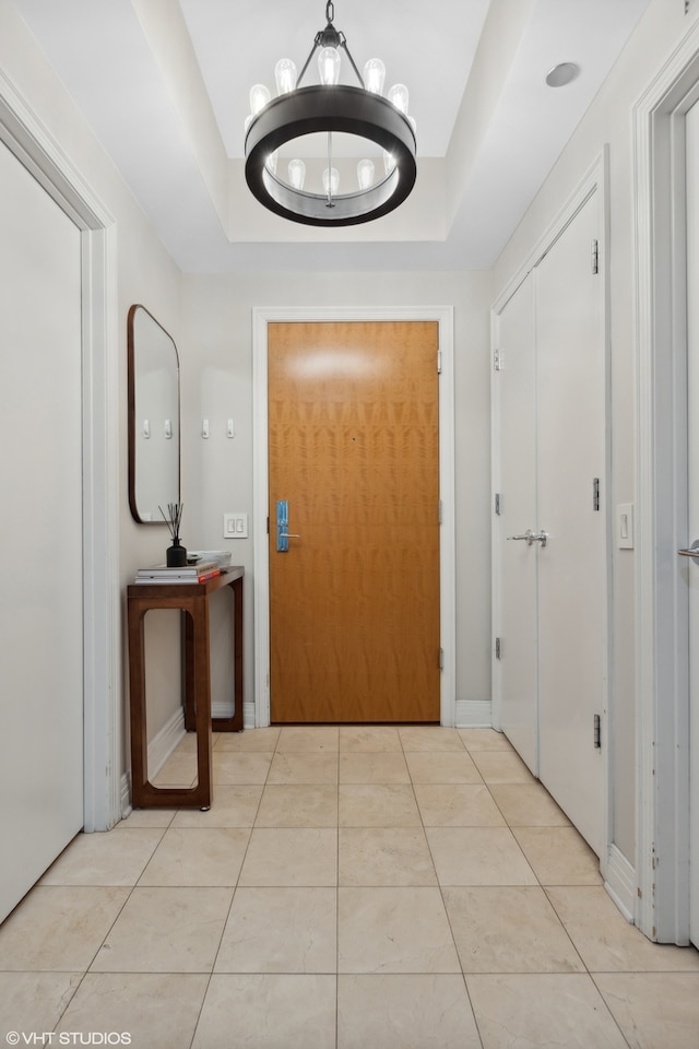 hall with a notable chandelier, light tile patterned floors, and a tray ceiling