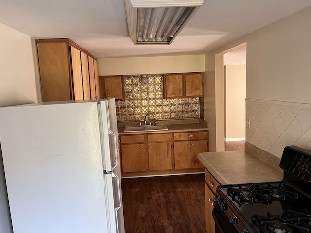 kitchen with sink, dark hardwood / wood-style flooring, tile walls, black gas range oven, and white refrigerator