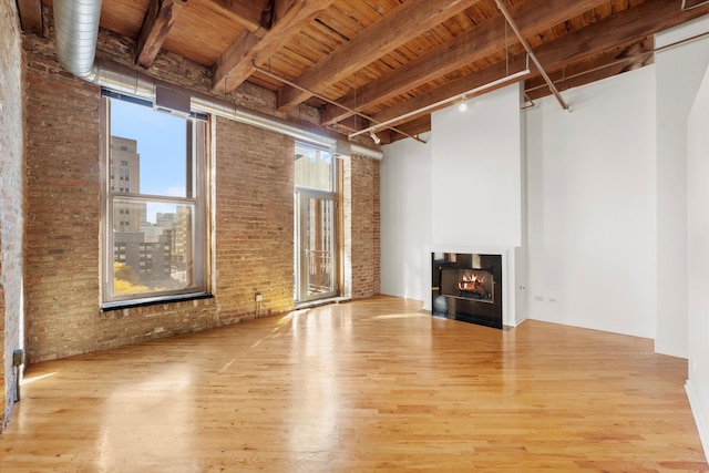 unfurnished living room with wood ceiling, brick wall, wood-type flooring, and beamed ceiling