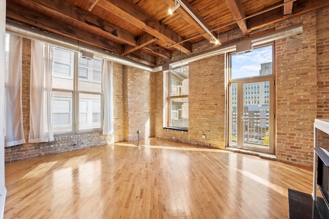 unfurnished living room featuring wood ceiling, hardwood / wood-style flooring, beam ceiling, and brick wall