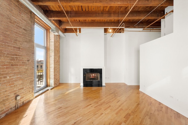 unfurnished living room featuring hardwood / wood-style floors, wooden ceiling, a high ceiling, beam ceiling, and brick wall