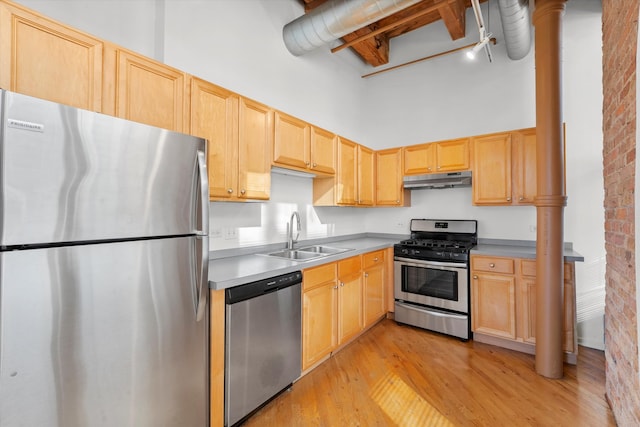 kitchen featuring a towering ceiling, appliances with stainless steel finishes, sink, light wood-type flooring, and brick wall