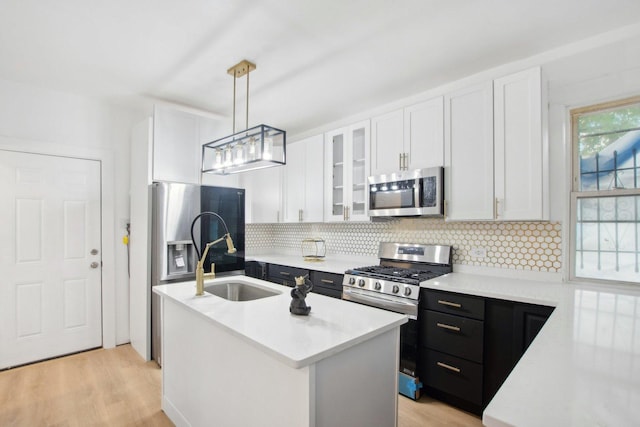 kitchen with stainless steel appliances, an island with sink, white cabinets, and light countertops