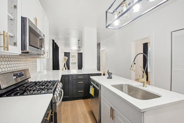 kitchen with a sink, appliances with stainless steel finishes, light countertops, and white cabinetry