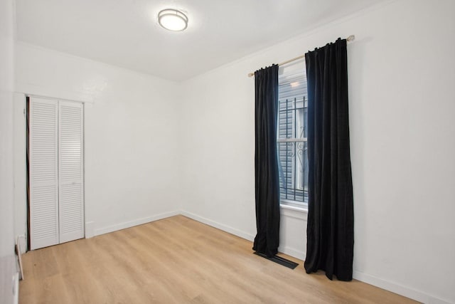 unfurnished bedroom with multiple windows, baseboards, light wood-type flooring, and a closet