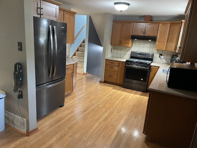 kitchen with stone countertops, backsplash, appliances with stainless steel finishes, and light hardwood / wood-style floors