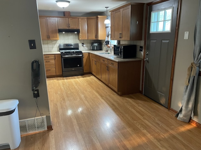 kitchen with backsplash, light hardwood / wood-style floors, hanging light fixtures, sink, and stainless steel gas stove