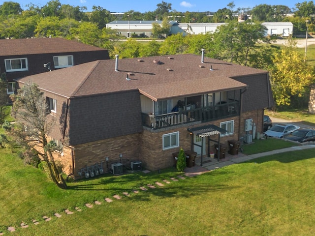 rear view of house featuring a balcony, cooling unit, a lawn, and a shingled roof