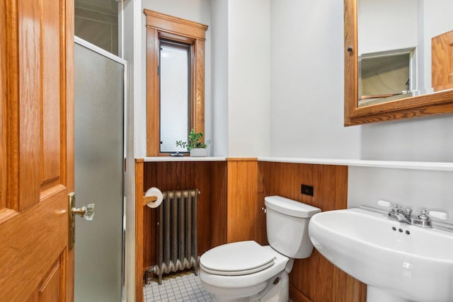 bathroom with radiator, sink, wooden walls, toilet, and walk in shower