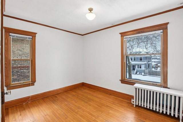 empty room with radiator heating unit, plenty of natural light, crown molding, and hardwood / wood-style floors