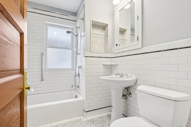 bathroom with tile patterned floors, tiled shower / bath combo, tile walls, and toilet